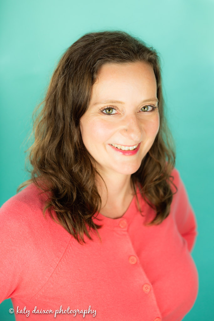 Sarah smiling in a pink sweater on teal back drop