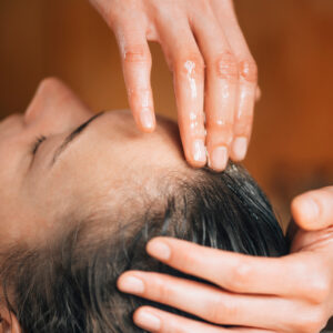 Massage therapist hand massage oil into female client's forehead and scalp
