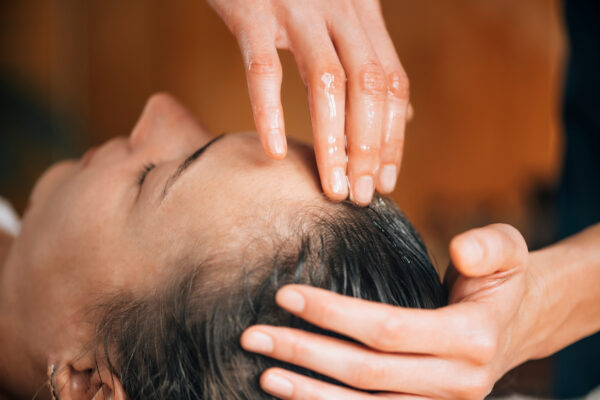 Massage therapist hand massage oil into female client's forehead and scalp
